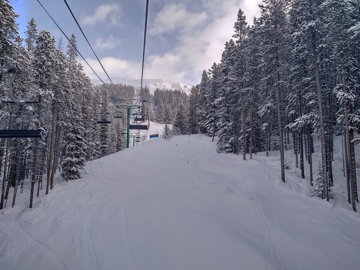 A chairlift line running through snow-covered spruce above a groomed run at Lake Louise Ski Resort