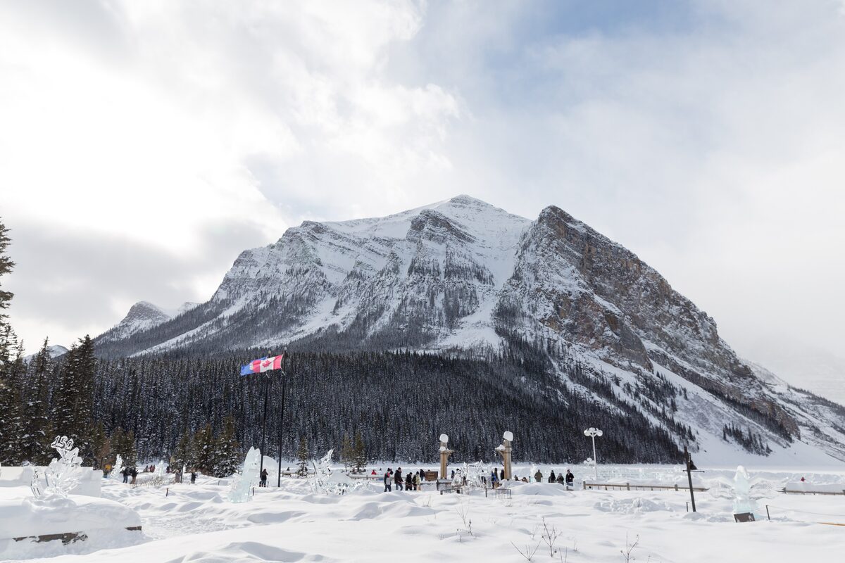 The frozen, snow-covered surface of Lake Louise with people far out on the ice below the Victoria massif