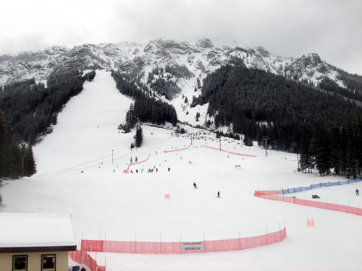 Snow-covered slopes at Mt Norquay with skiers on the lower runs, a red-netted race course and rocky peaks behind