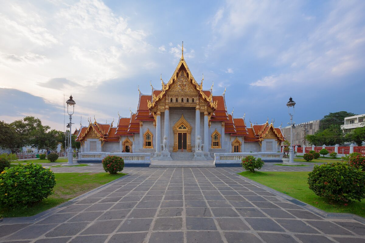 The white Carrara marble facade of Wat Benchamabophit, the Marble Temple, with lawns and lamp posts in front