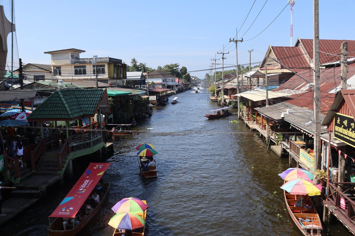 Boats with colorful parasols on the canal at the Damnoen Saduak floating market, seen from a bridge between wooden market houses