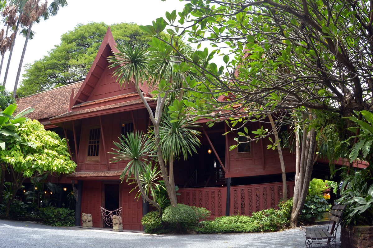 The main house of the Jim Thompson House, a red teak Thai-style home among palms and tropical trees