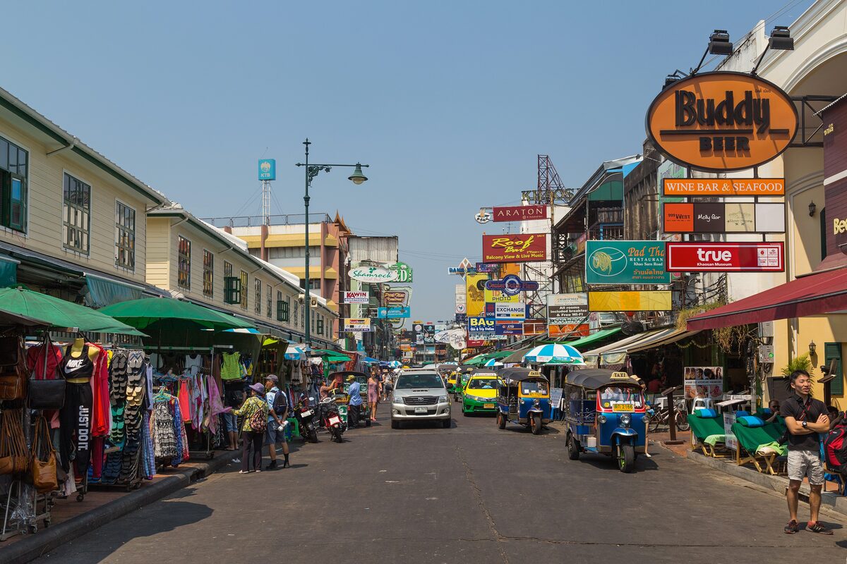 Khao San Road with tuk-tuks, clothing stalls and shopfronts with signs lining the street