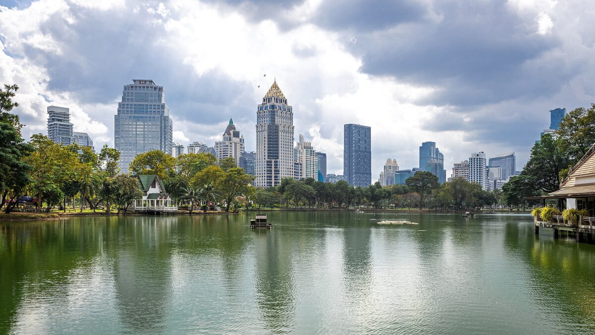 The lake in Lumphini Park with tree-lined shores and the towers of the business district rising behind it