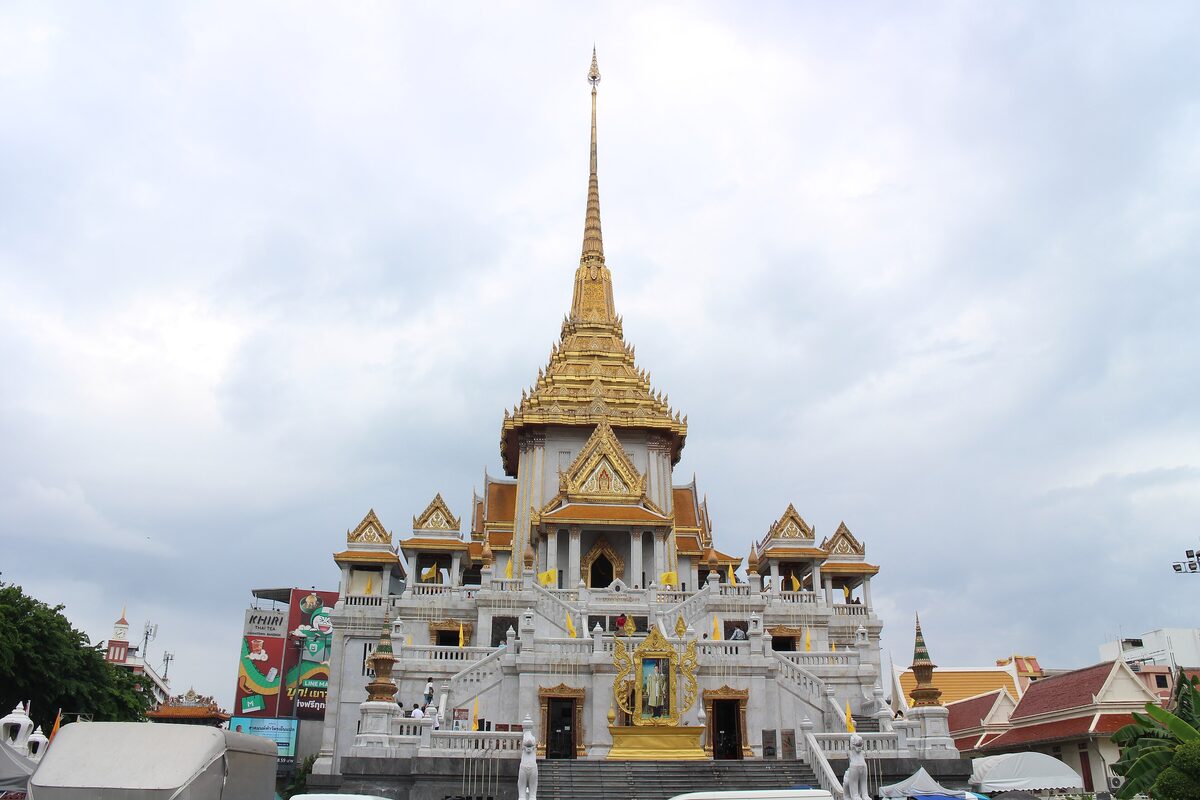 The white and gold temple building of Wat Traimit with its tall gilded spire, seen from the street