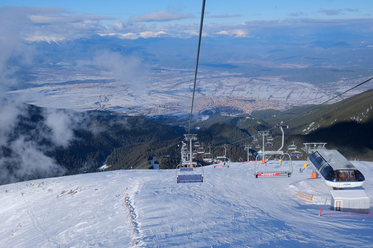 A chairlift climbing a wide snowy slope toward a ridge in the Bansko ski area