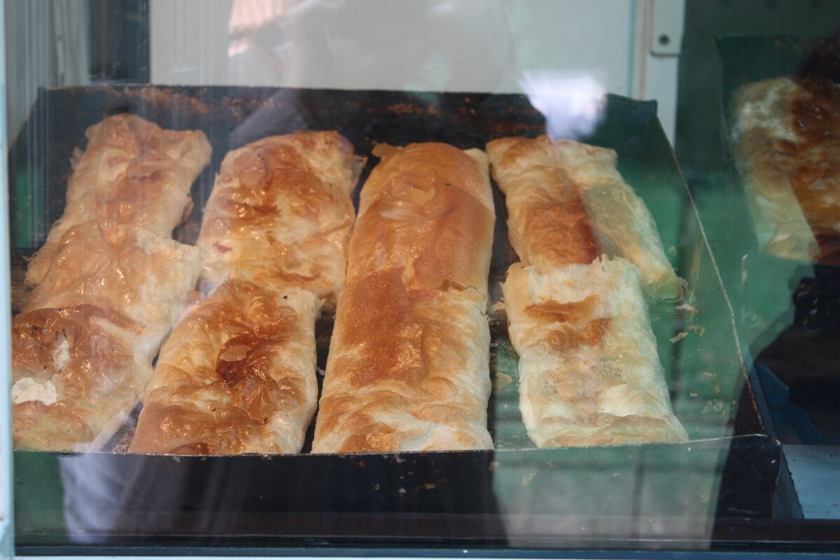 Trays of golden baked banitsa, flaky pastry rolls, behind the glass of a bakery counter