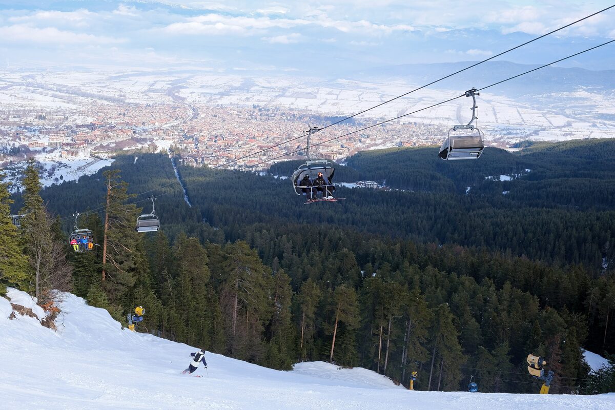 The Chalin Valog chairlift above a snowy slope and pine forest, with the town of Bansko in the valley far below