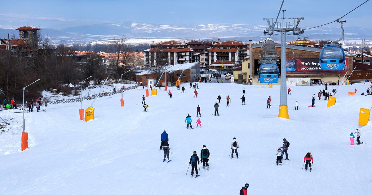 Skiers on the snow below the Bansko gondola station, with cabins overhead and the town behind