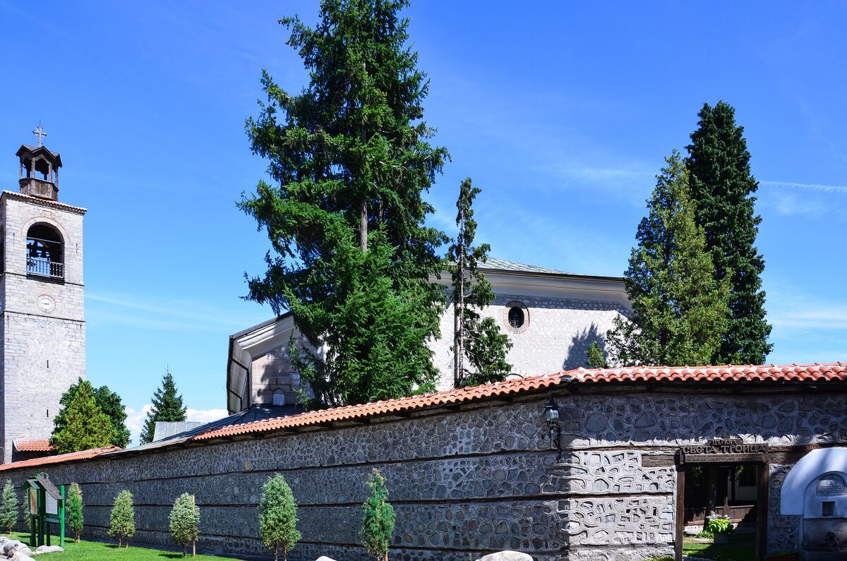 Holy Trinity Church in Bansko with its stone bell tower and the courtyard wall, under a blue sky