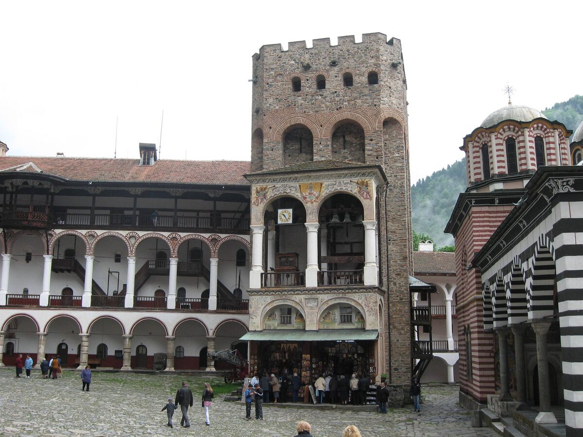 Hrelyo's Tower rising over the arcaded galleries of the Rila Monastery courtyard, with visitors below