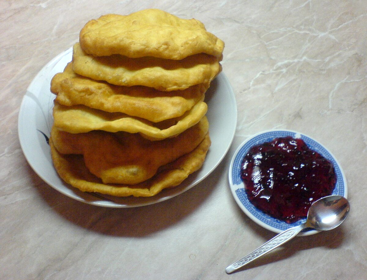 A stack of fried mekitsi on a plate with a bowl of plum jam beside it