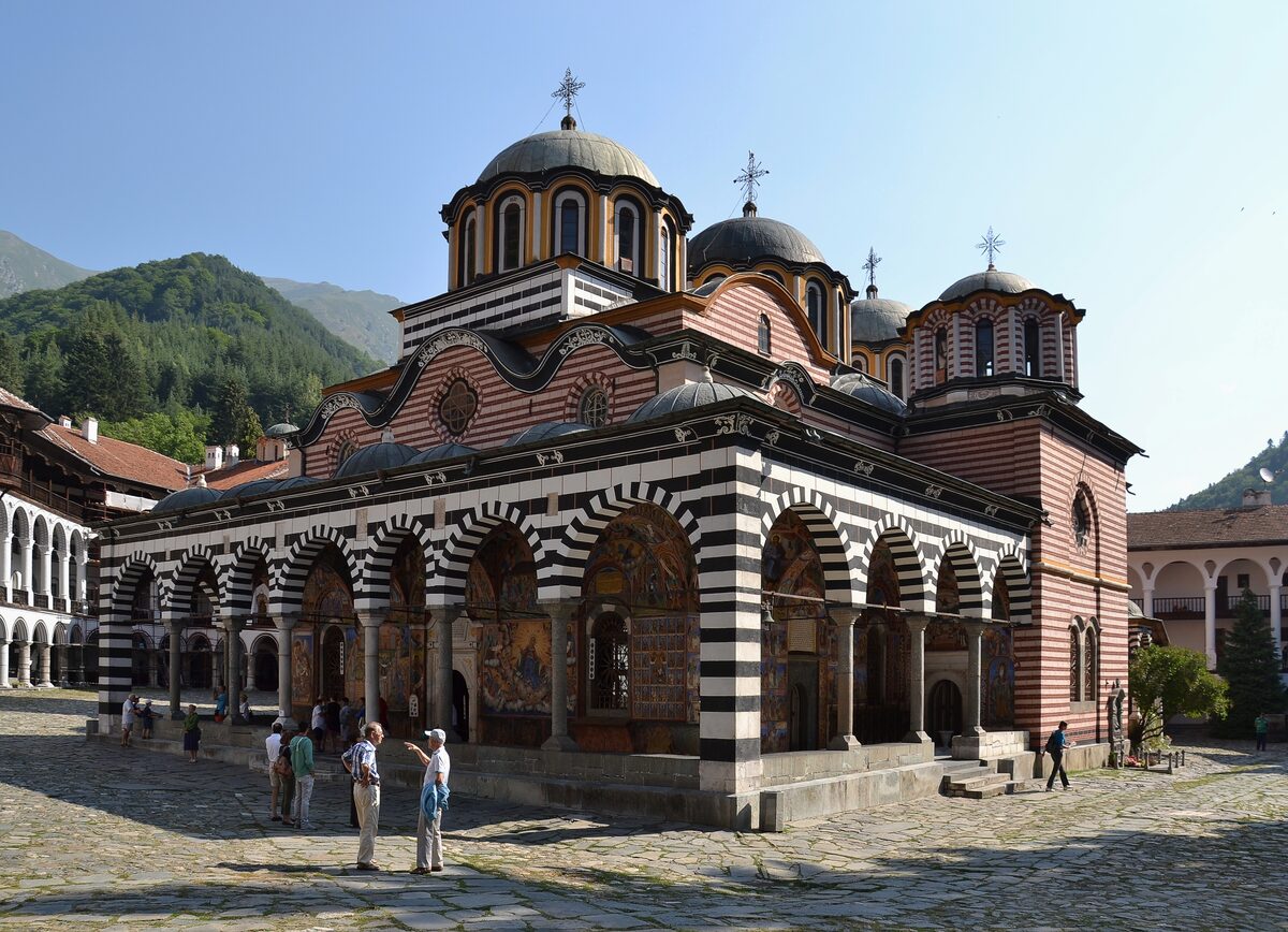 The main church of Rila Monastery with its red and white striped arches, domes and crosses in the courtyard