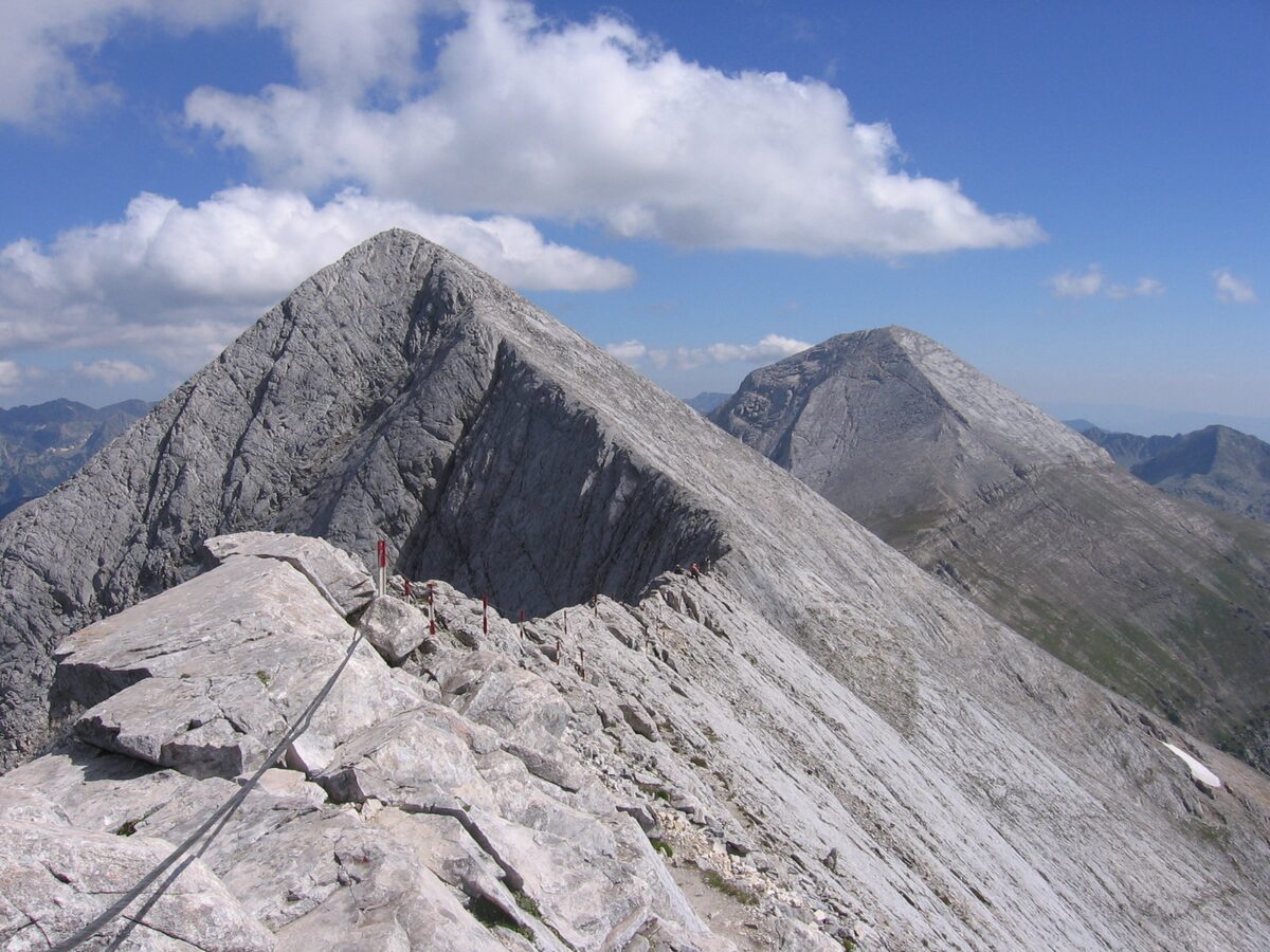 A pale limestone ridge with a secured path along the Koncheto crest, Kutelo ahead and Vihren behind, in the Pirin Mountains in summer