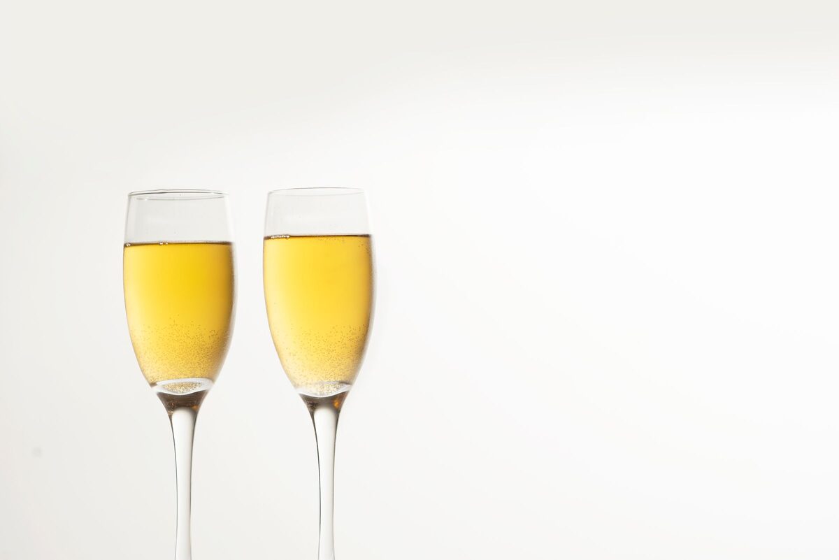 Two flutes of chilled sparkling white wine against a white background