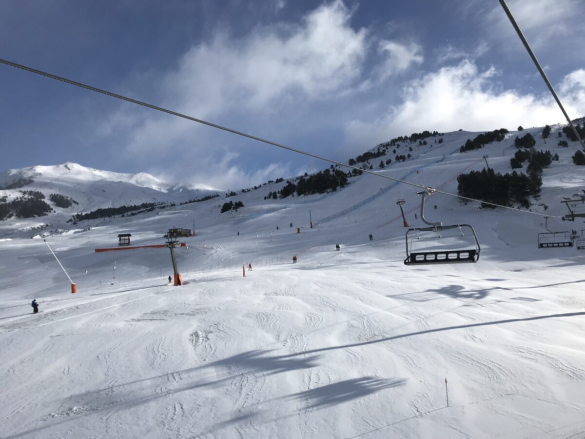 Wide groomed slopes with a chairlift and skiers under scattered clouds at Baqueira-Beret