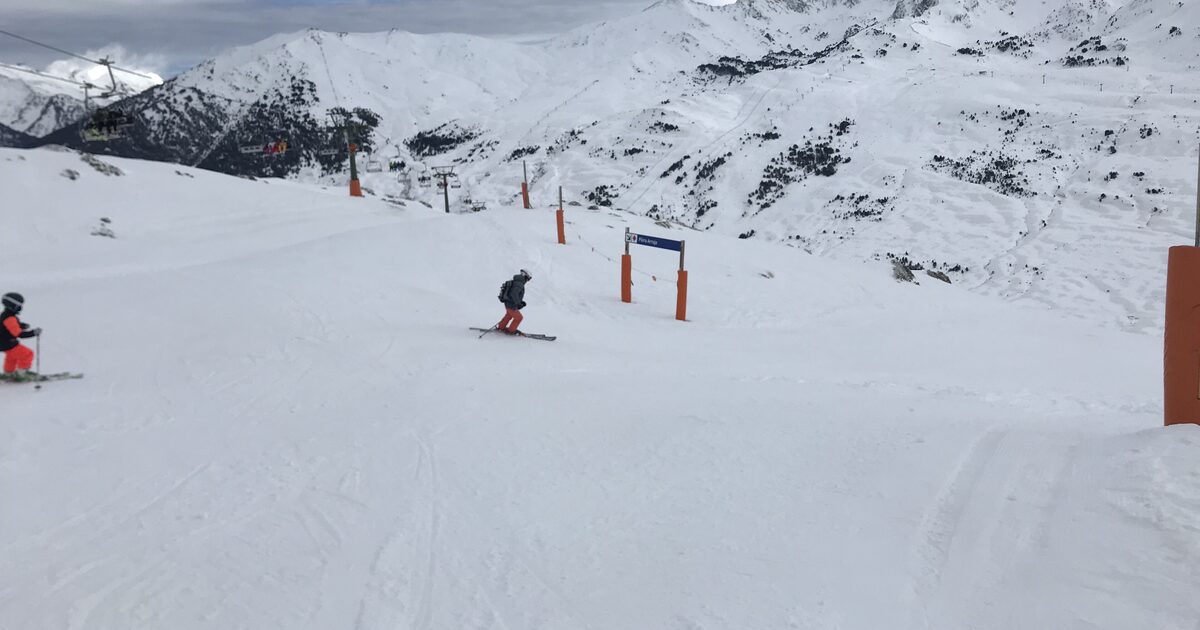 A skier on a groomed Baqueira Beret piste with orange gates and snowy peaks behind