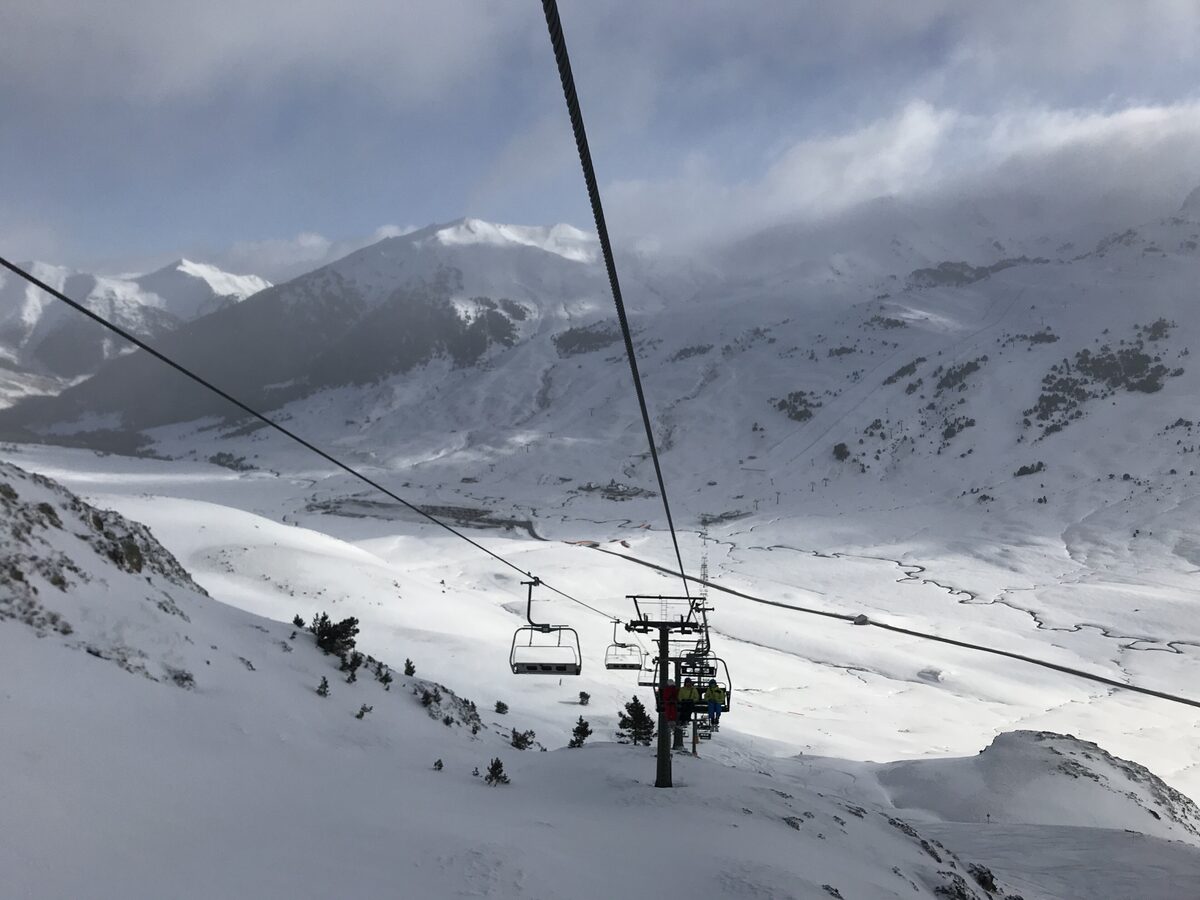 A chairlift with skiers crossing a snowy valley below mountains and cloud at Baqueira-Beret
