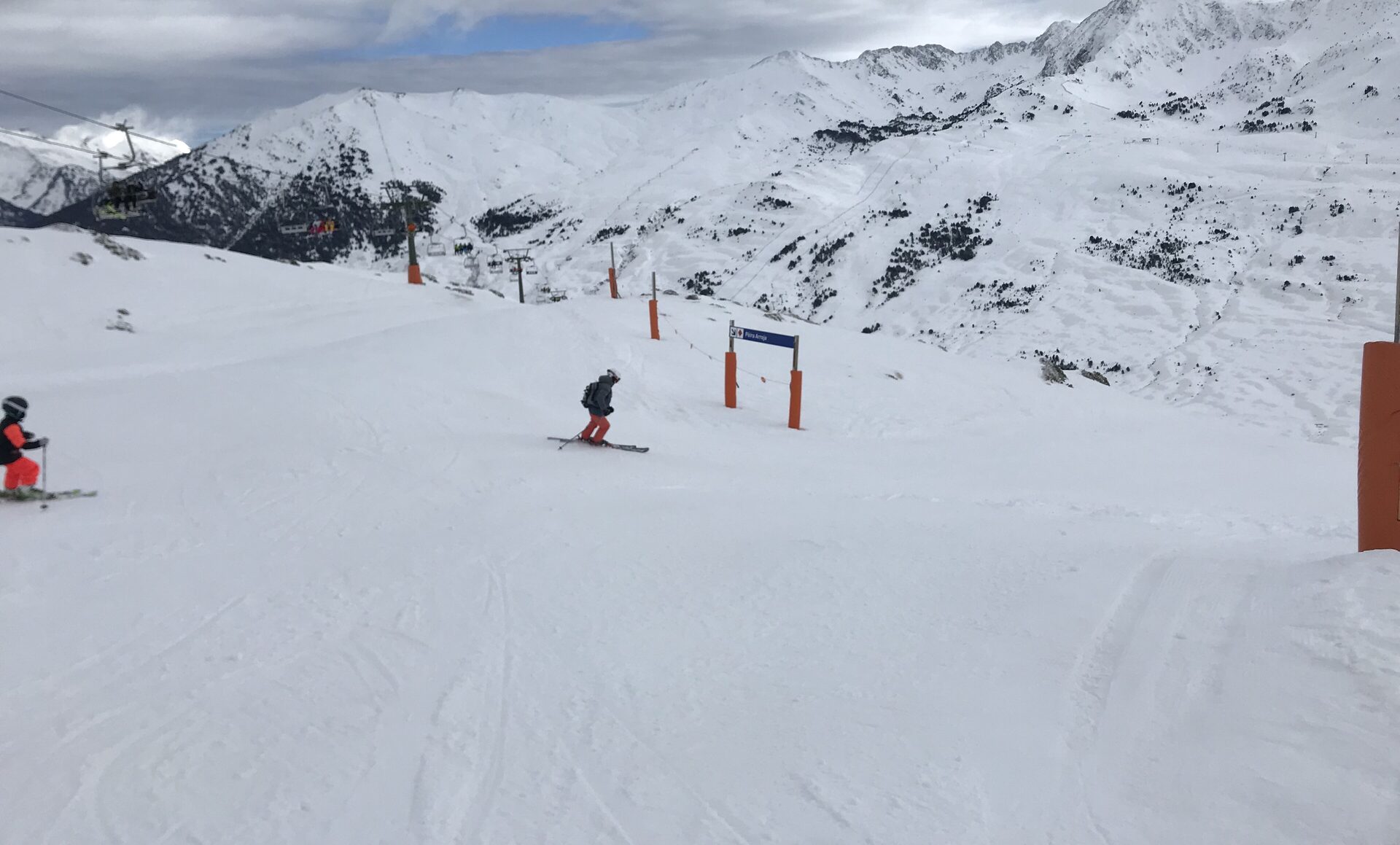 A skier on a groomed Baqueira Beret piste with orange gates and snowy peaks behind