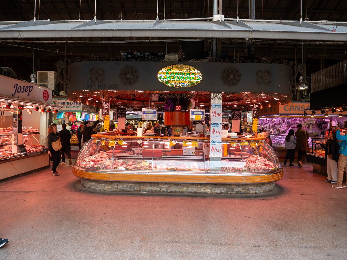 A meat counter inside La Boqueria market with shoppers between the stalls