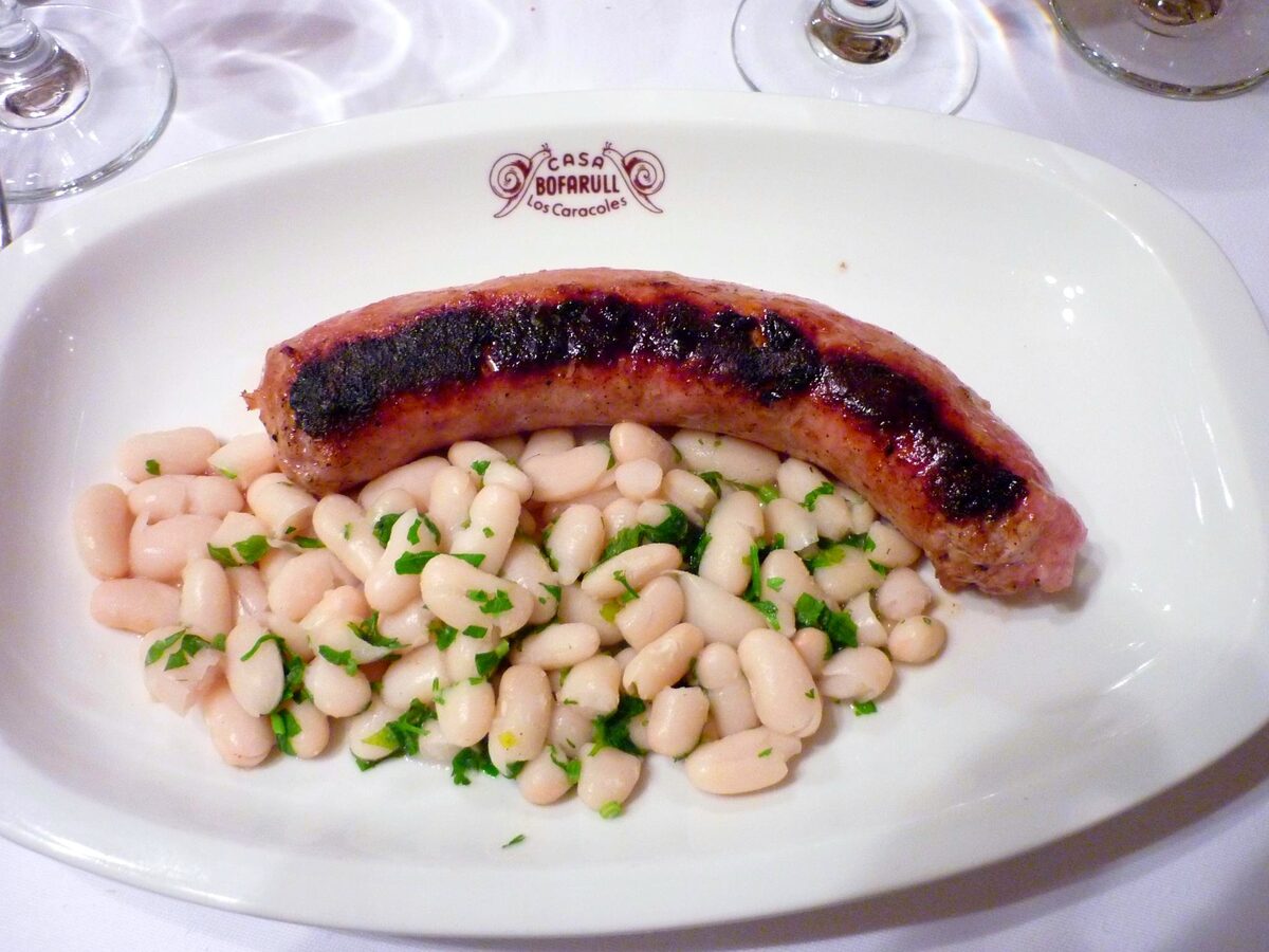 A grilled botifarra sausage on a bed of white beans