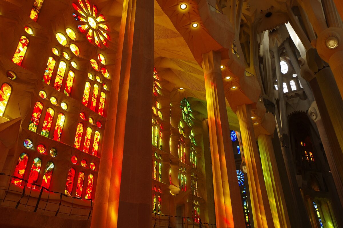 Coloured light from stained-glass windows between the branching columns of the Sagrada Família