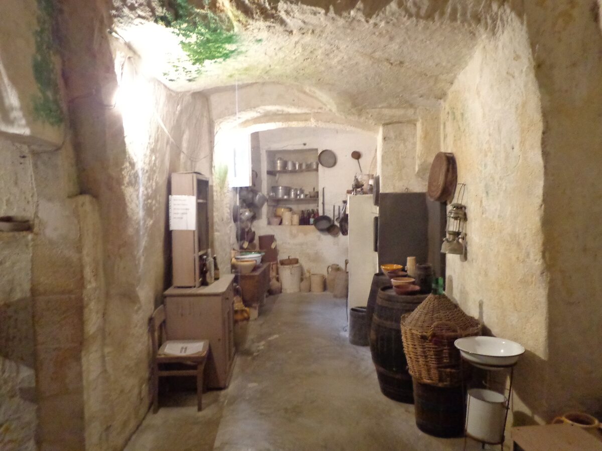 Inside a rock-cut Casa Grotta, a kitchen with barrels, baskets and a worn stone floor