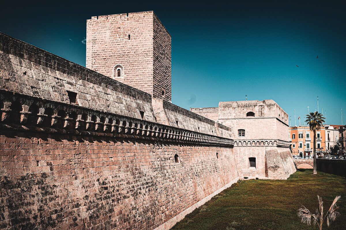 The moat and the square tower of the Norman-Swabian castle, with the stone curtain wall running along the grass