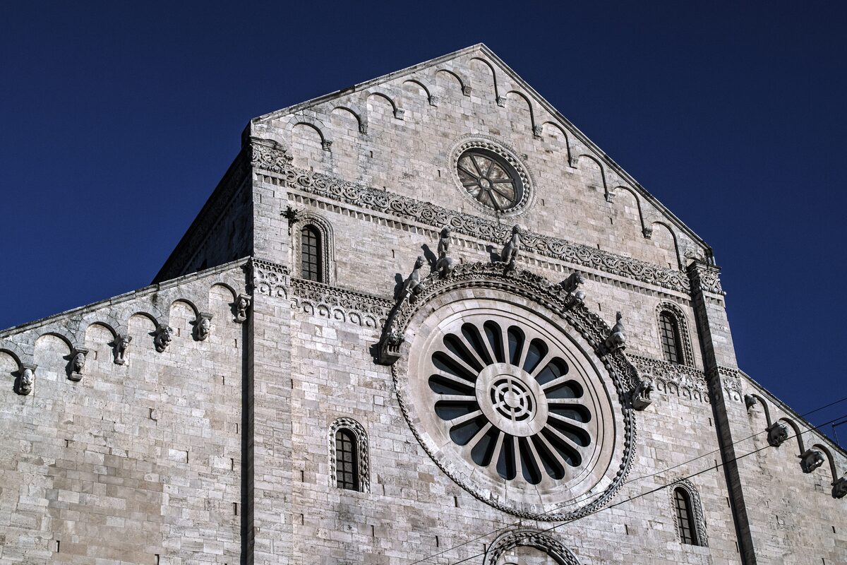The stone facade of Bari Cathedral with its rose window and arcaded gable, in bright sunlight