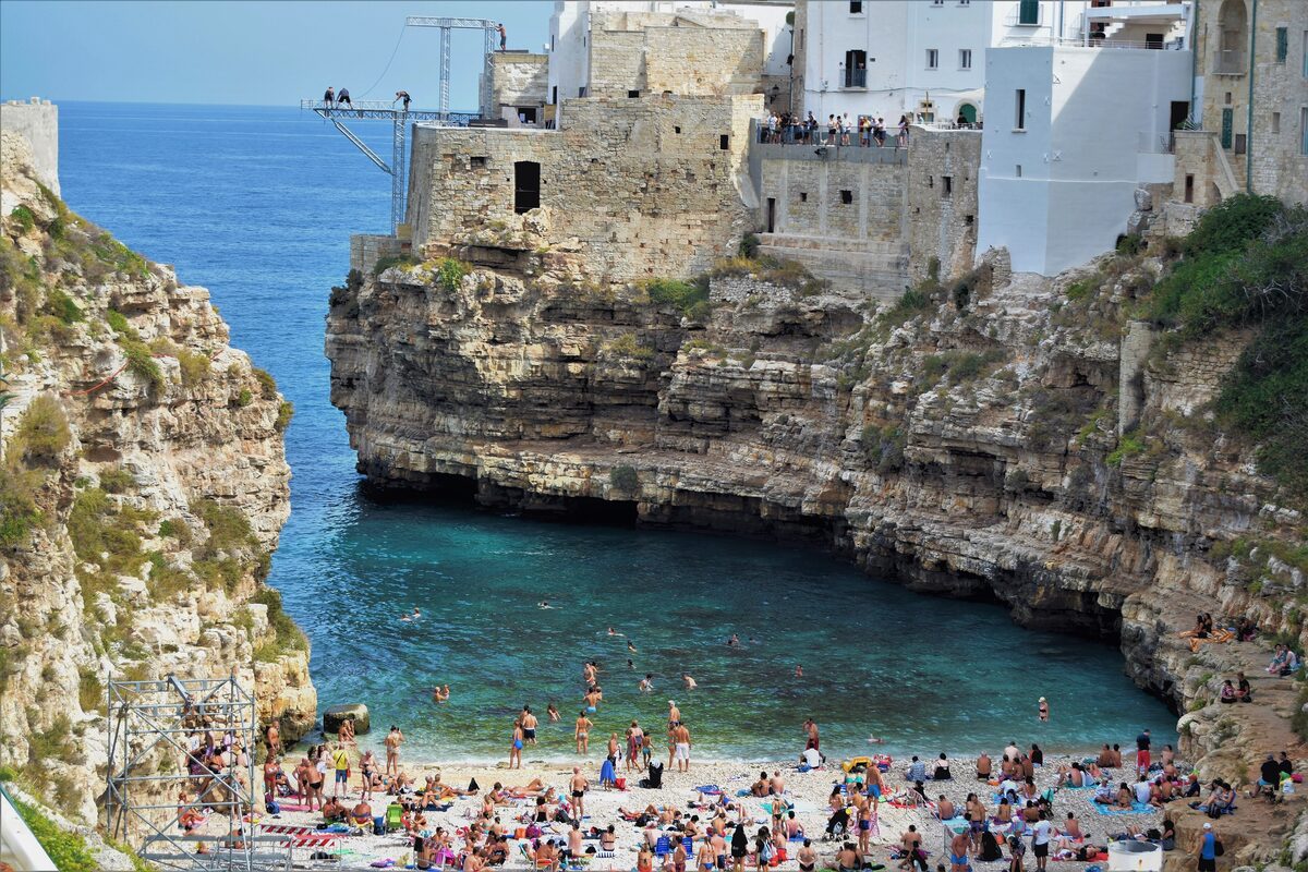 Lama Monachile in summer, with people on the pebble beach at the end of the cove and old houses on the cliffs