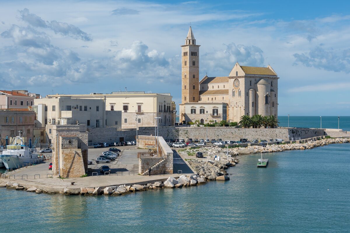 Trani cathedral and its bell tower on the water's edge, seen across the harbour
