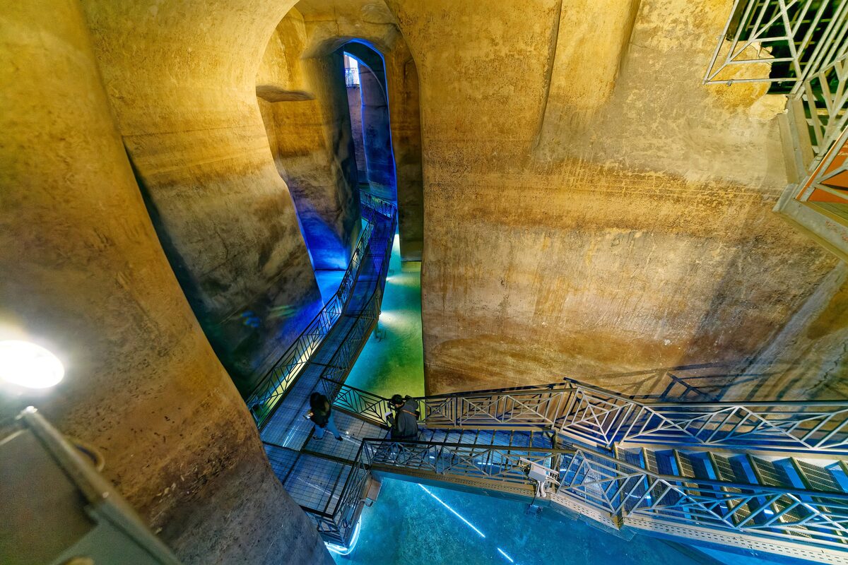 Inside the Palombaro Lungo, the huge rock-cut cistern under Piazza Vittorio Veneto, with a walkway above the blue-lit water