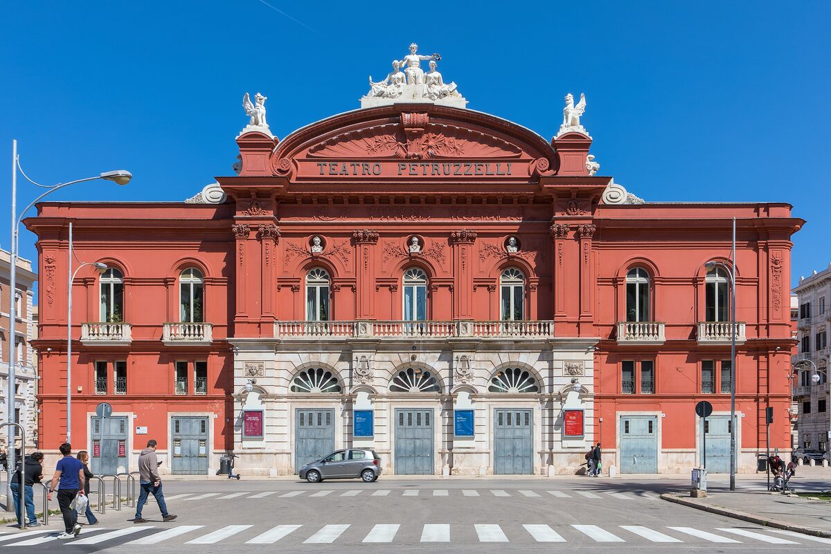 The red facade of the Teatro Petruzzelli with its white statues on the roofline, seen across the square