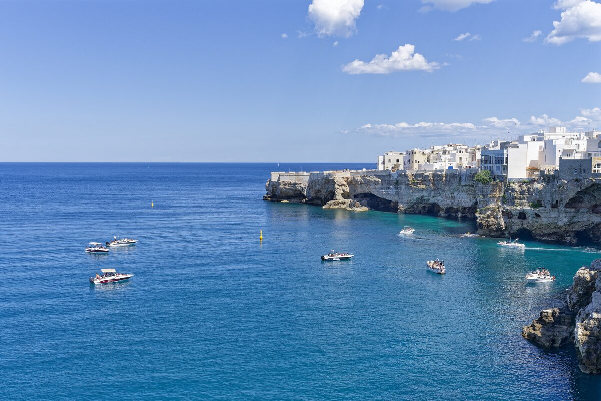 The white houses of Polignano a Mare on the cliff edge above the blue Adriatic, with small boats below