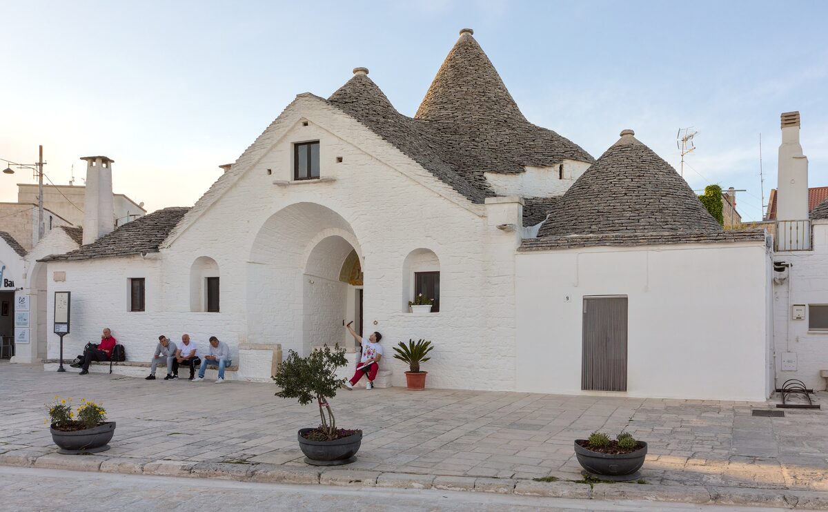 The Trullo Sovrano in Alberobello, a white two-storey trullo with its cone roofs in late afternoon light
