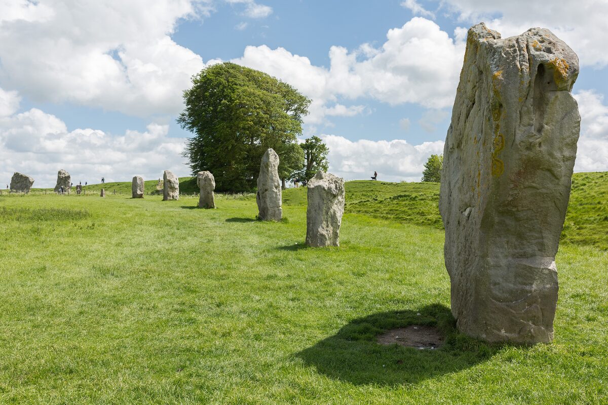Large standing stones in a grassy field at Avebury, with a village house behind