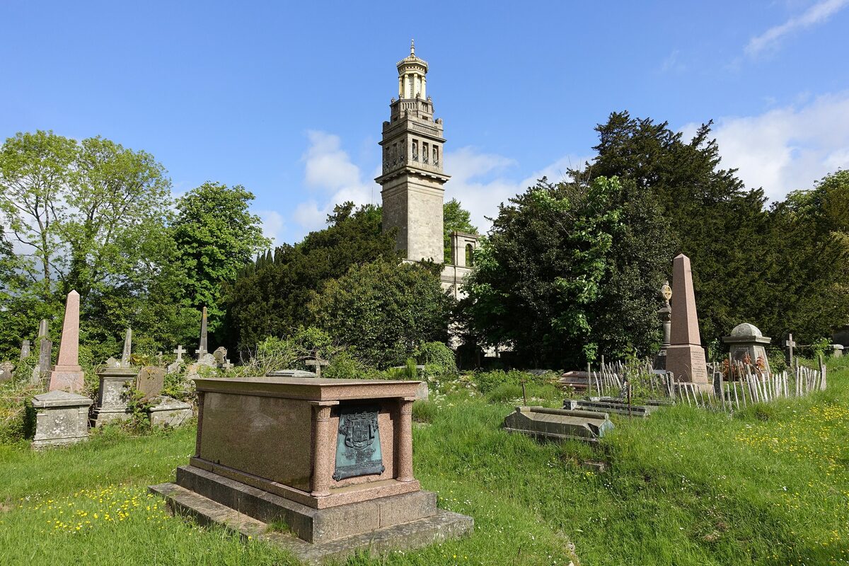 Beckford's Tower, a tall stone tower with a gilded lantern on top, above trees and gravestones on Lansdown hill
