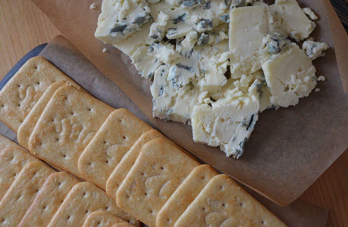 Crumbled blue cheese and a white cheese on paper beside rows of square crackers