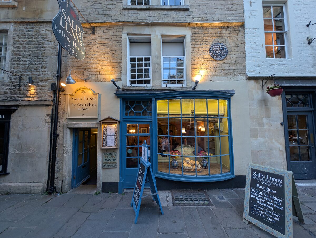 The narrow old stone house of Sally Lunn's Eating House on a lane in Bath, with a green shopfront and window boxes