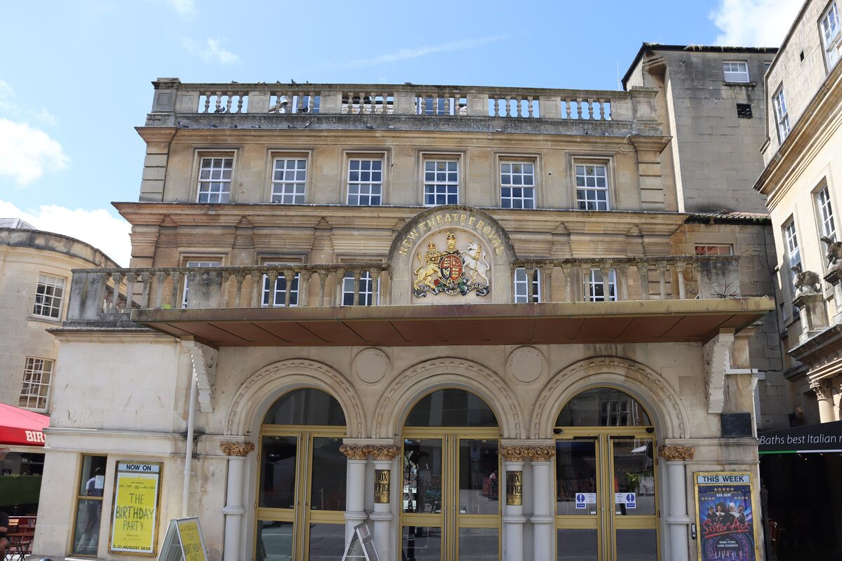 The Georgian stone front of the Theatre Royal in Bath, with arched doors and a royal coat of arms above