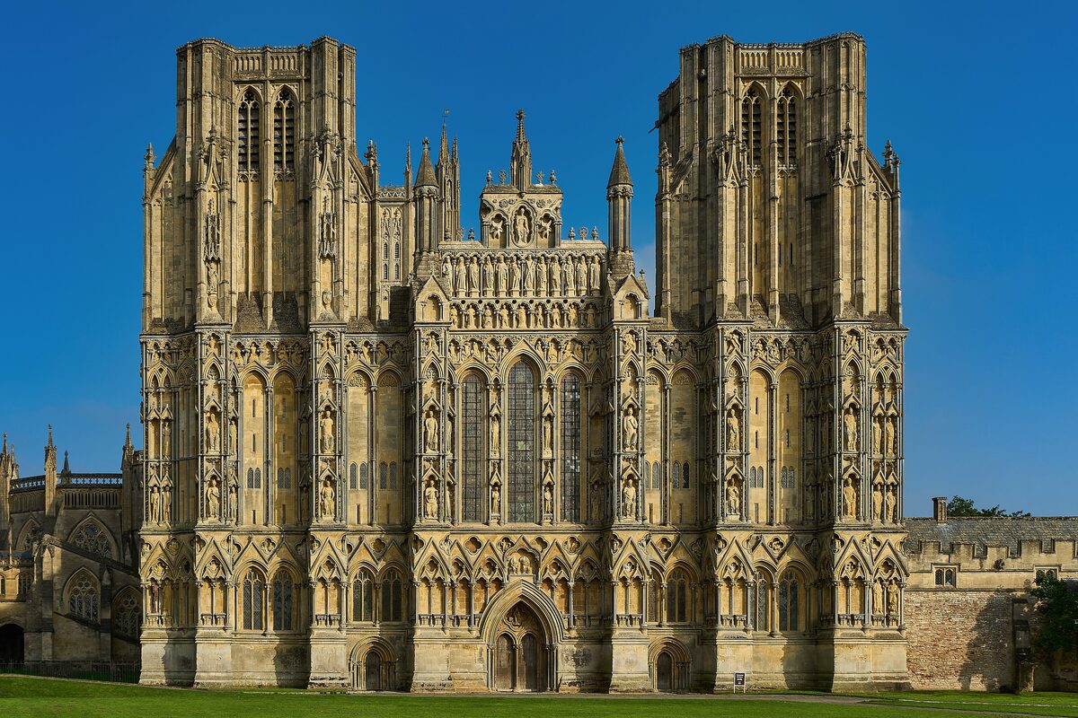 The west front of Wells Cathedral, covered in rows of medieval statues, under a deep blue sky