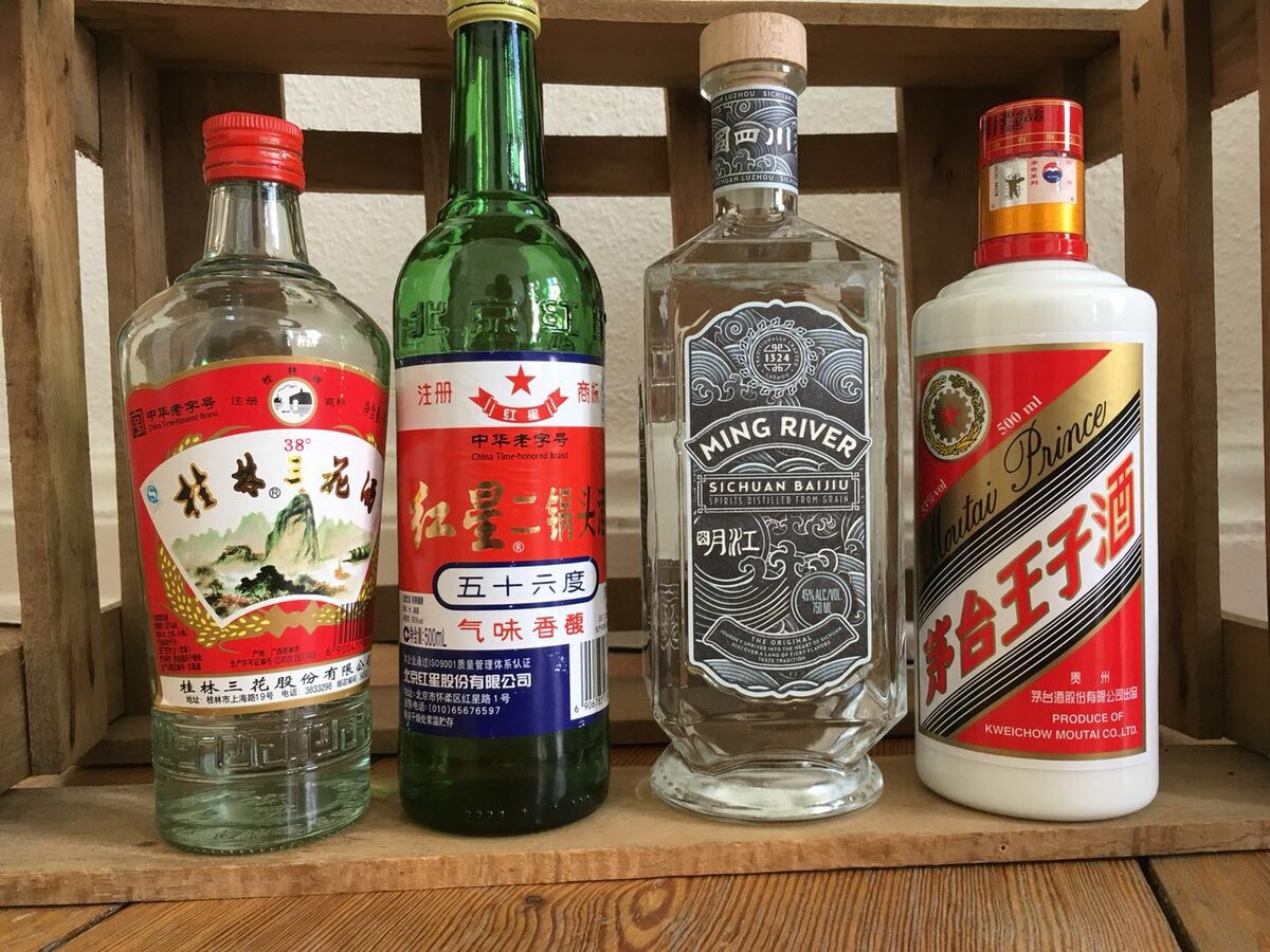 Four baijiu bottles on a wooden shelf, among them the green bottle of Red Star erguotou with its red star label
