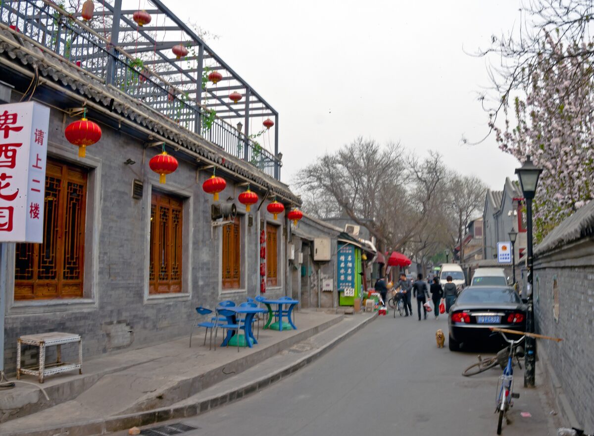A sidewalk cafe with blue tables on a quiet hutong lane lined with red lanterns and gray brick walls