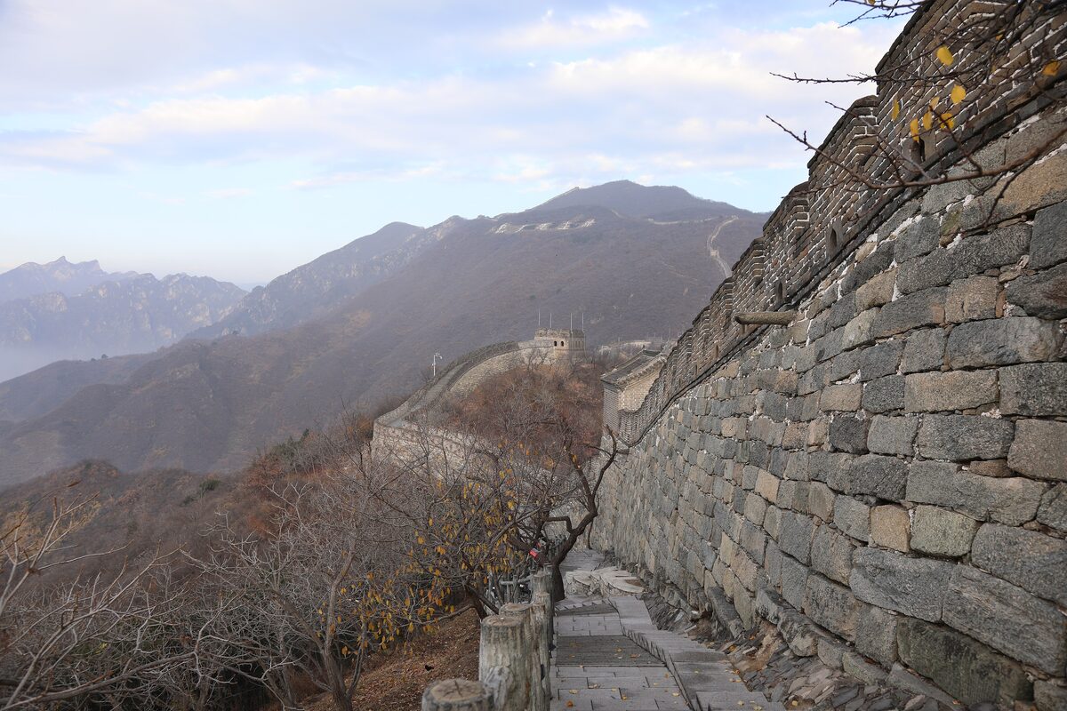 The stone wall at Mutianyu climbing a mountain ridge toward a distant watchtower under a pale blue sky