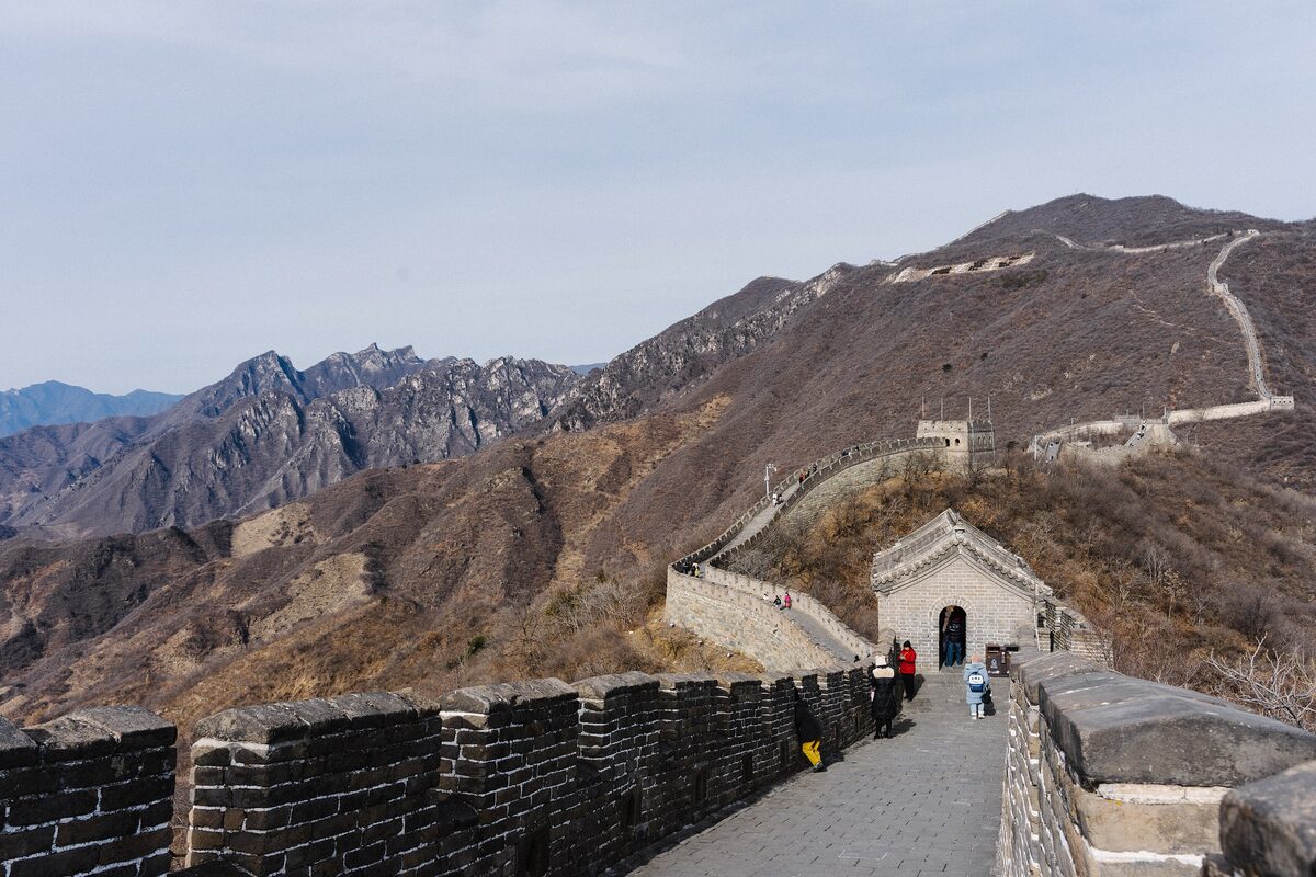 The Great Wall at Mutianyu running along a mountain ridge with several watchtowers, and walkers on the path