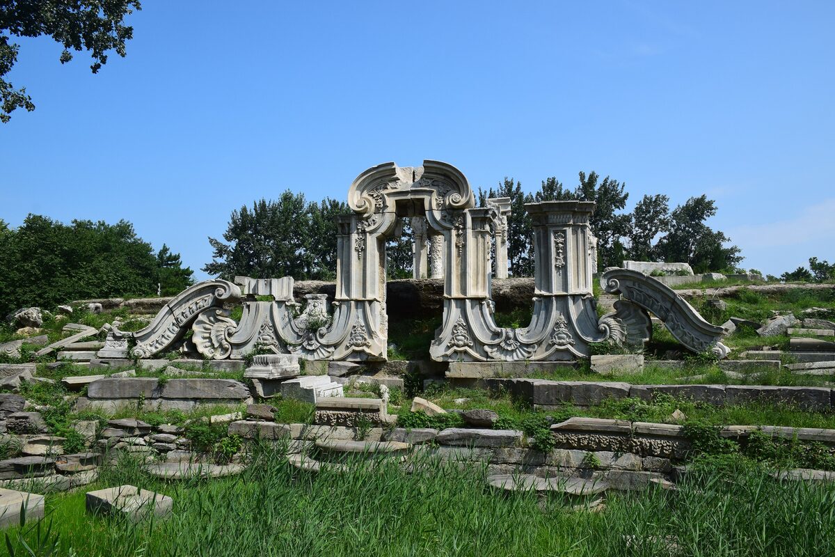 The carved white marble ruins of the Dashuifa fountain in the Old Summer Palace, in a green park under a blue sky