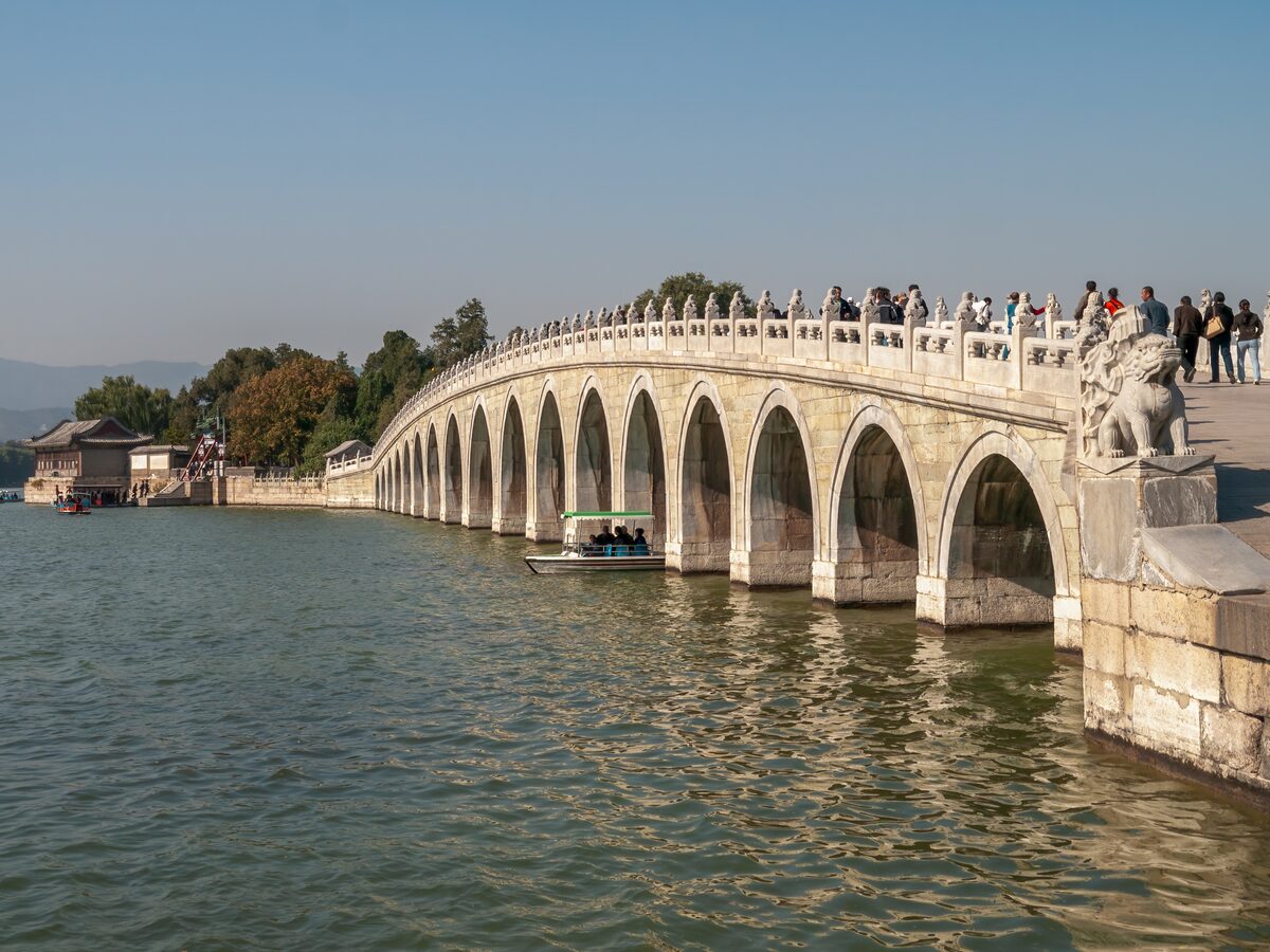 The Seventeen-Arch Bridge crossing Kunming Lake, with a stone lion in the foreground and visitors on the bridge