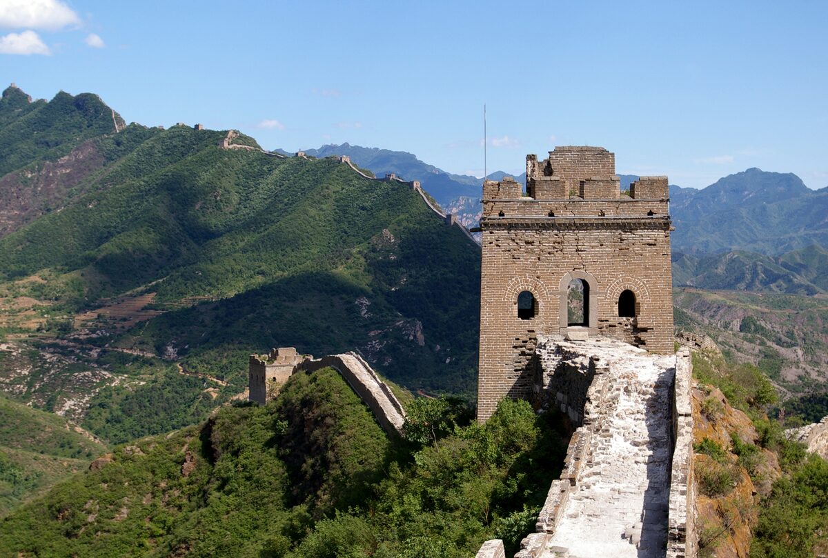 A crumbling stone watchtower on the unrestored Simatai section of the Great Wall, with green hills behind