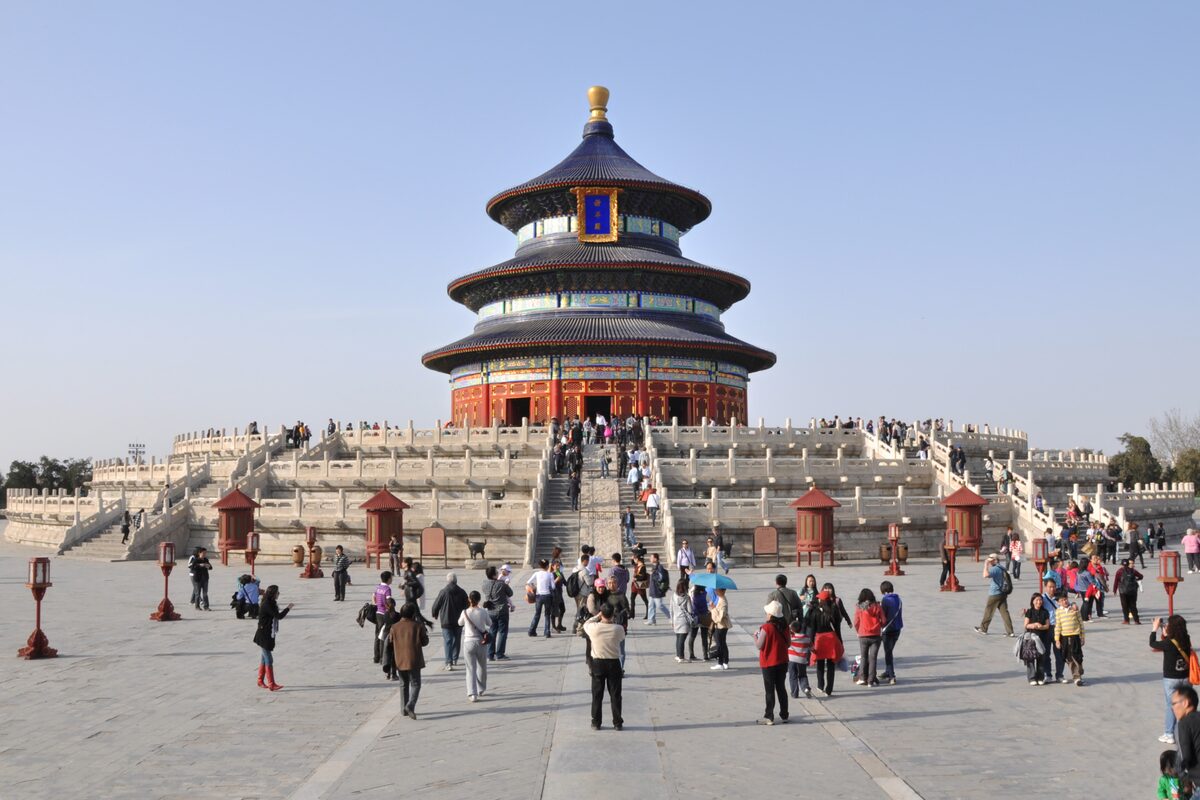 The round Hall of Prayer for Good Harvests with its three blue roofs on a white marble terrace, visitors on the steps in front