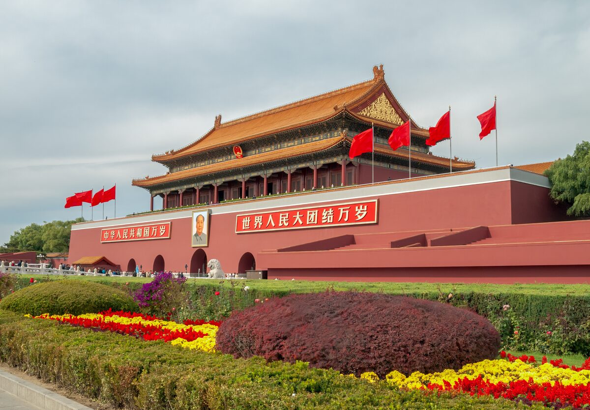 The red Tiananmen gate tower with its double yellow-tiled roof, flags and flowerbeds in front